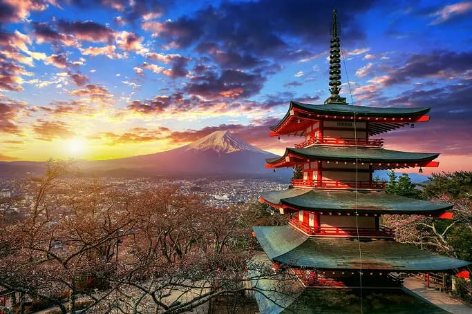 A red pagoda at sunset with Mount Fuji behind it