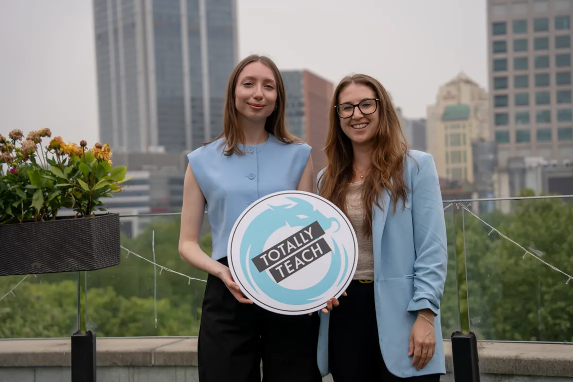Rose and Rowena holding a Totally Teach sign on a city rooftop